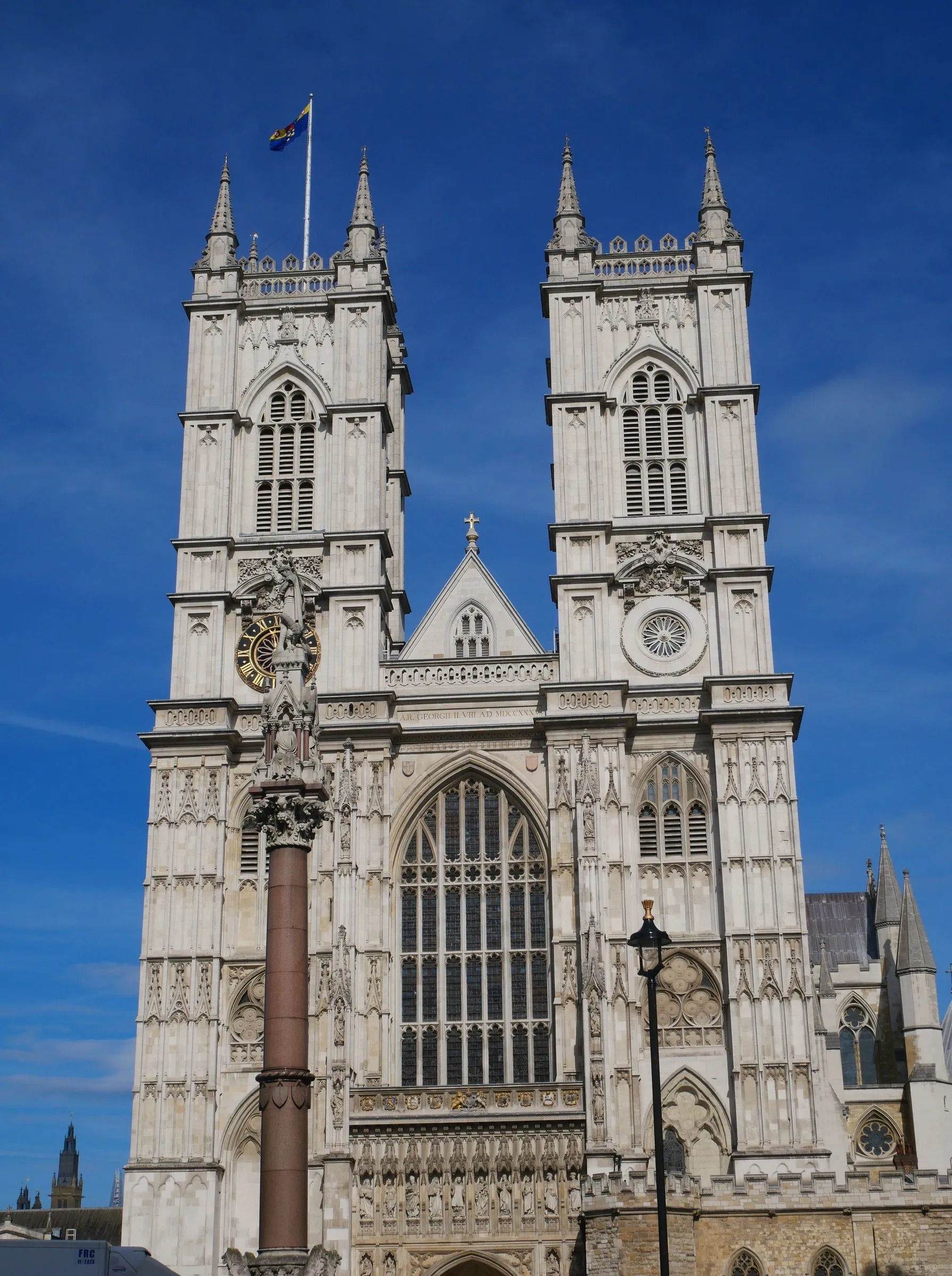 Fachada oeste da Abadia de Westminster com as duas torres góticas, vista de baixo contra um céu azul intenso.