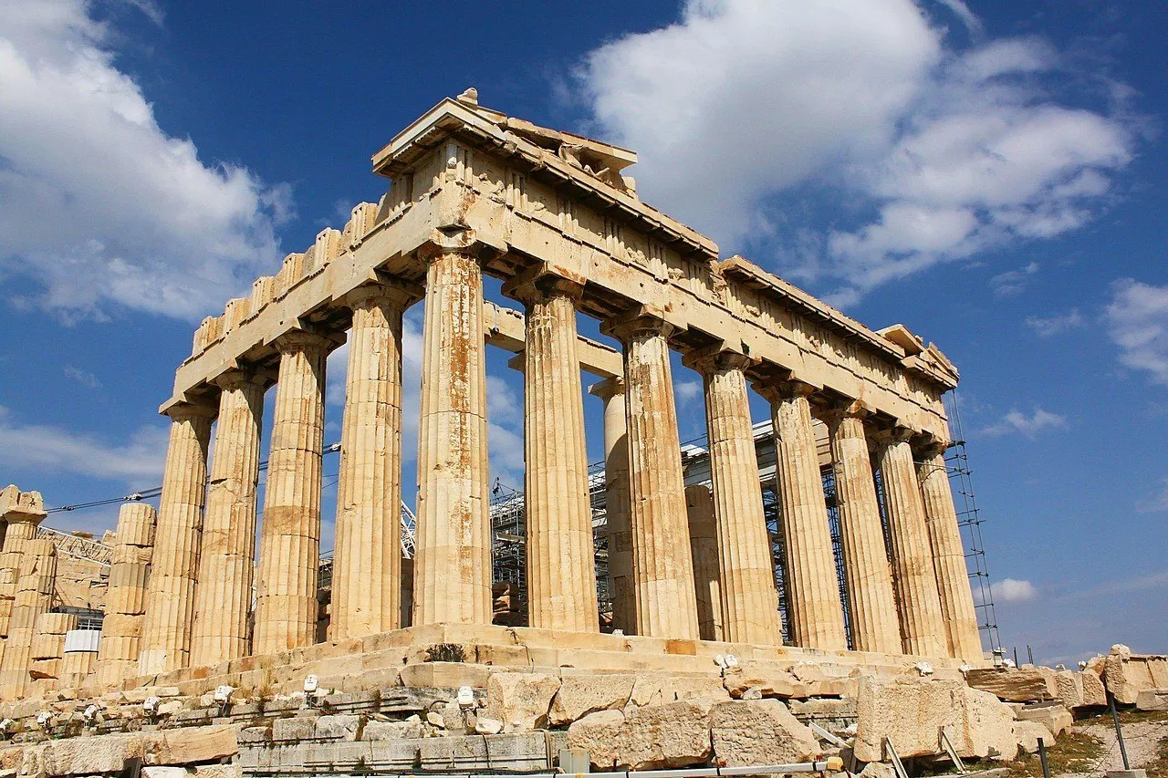 Exterior do Partenon na Acrópole de Atenas, com colunas de mármore sob céu azul com nuvens.