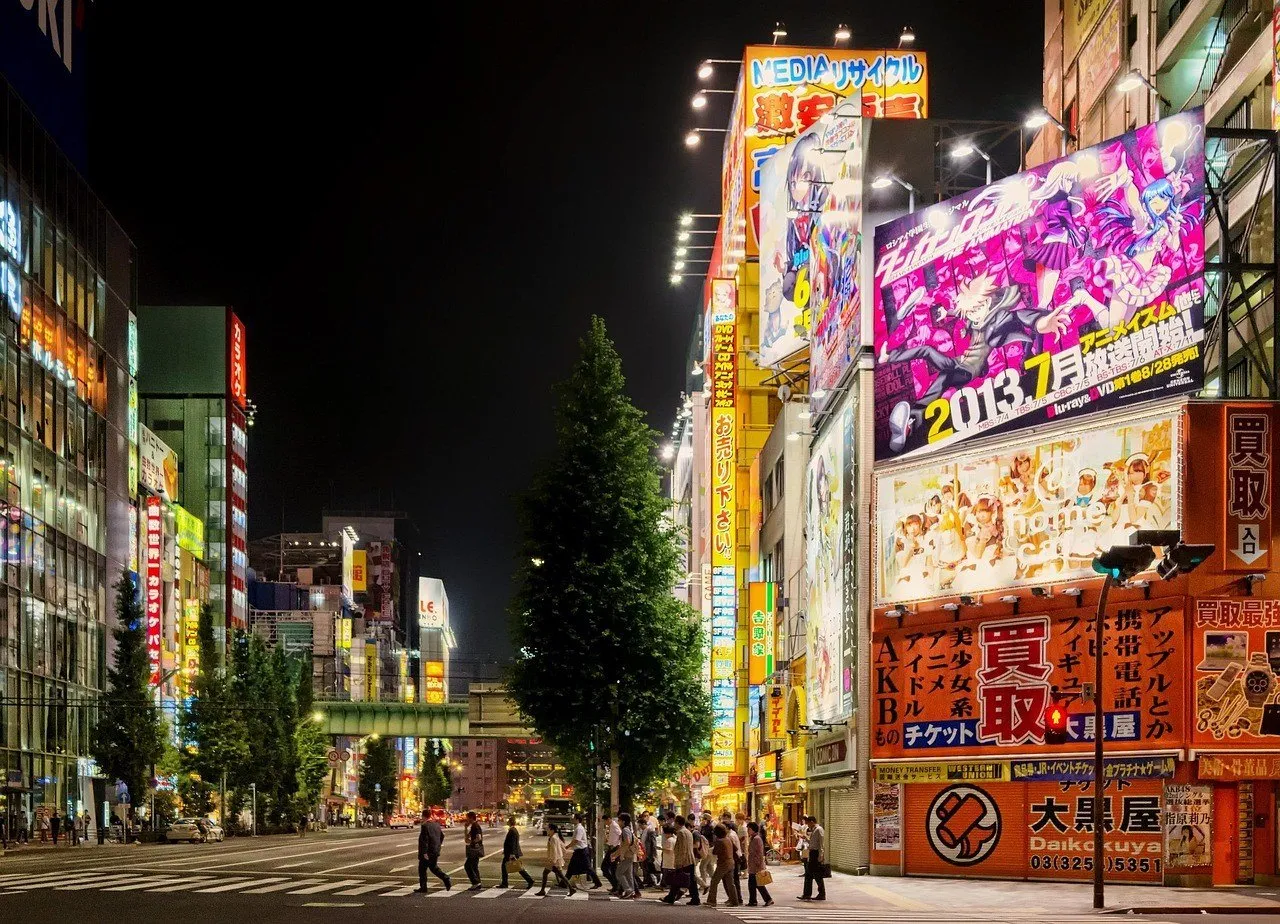 Rua de Akihabara à noite, com letreiros luminosos, prédios comerciais e pedestres atravessando.