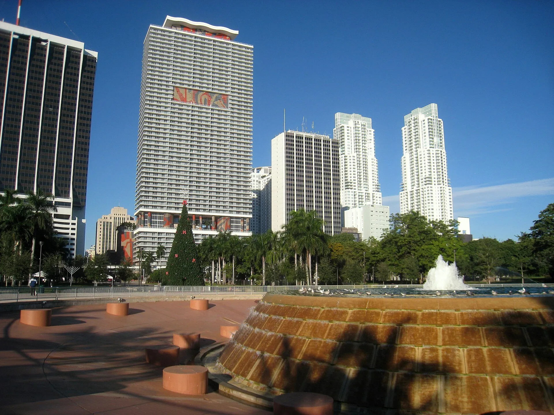 Fonte circular do Bayfront Park, em Miami, com árvores, decoração de Natal e prédios de Downtown ao fundo.