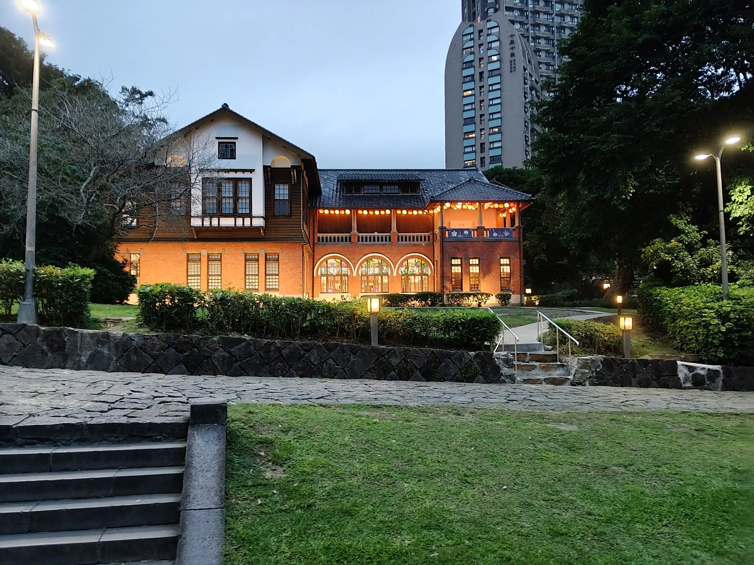Museu das Fontes Termais de Beitou iluminado ao anoitecer, com jardim e caminhos em primeiro plano.