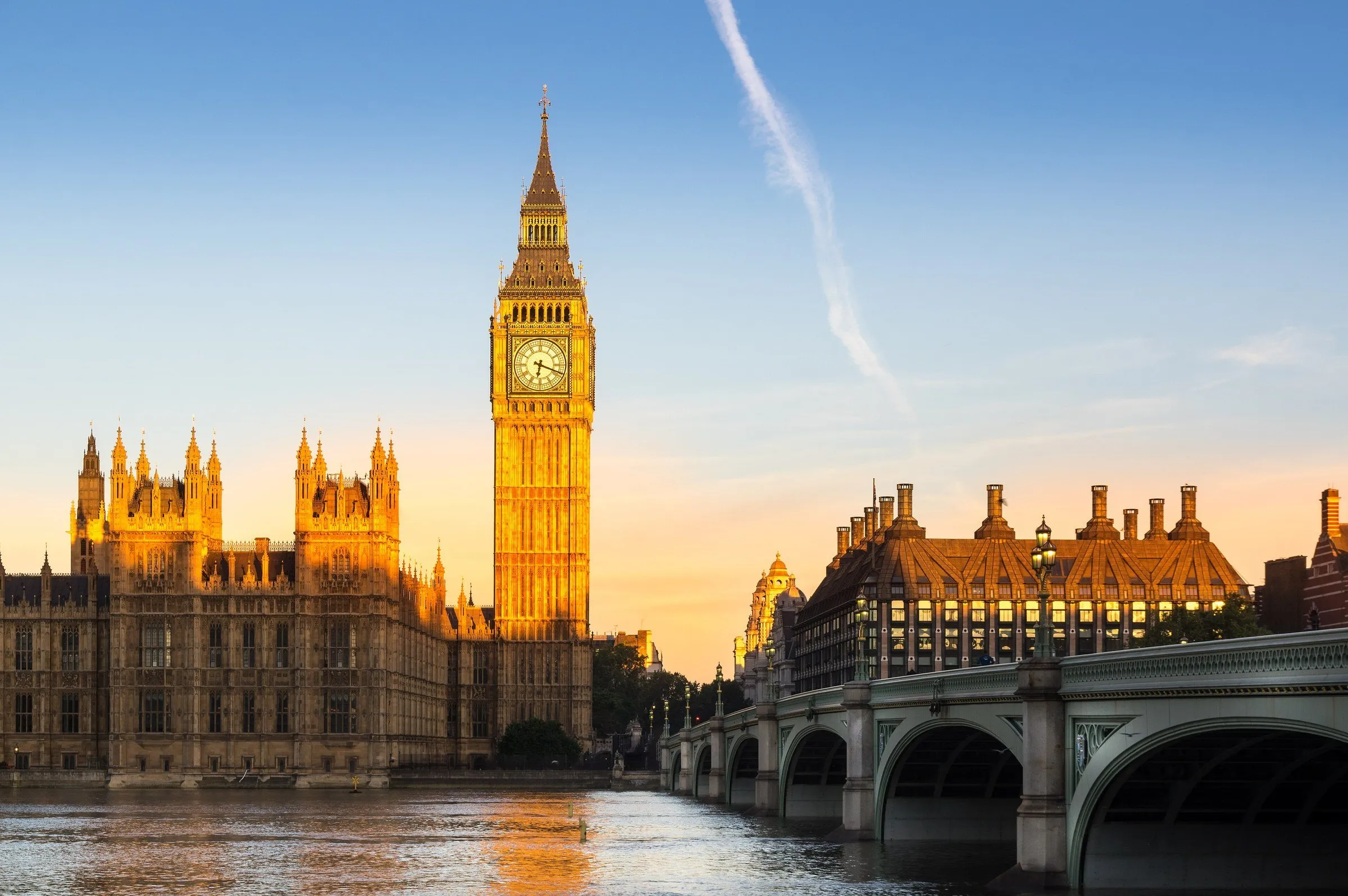 Elizabeth Tower e Palácio de Westminster iluminados pelo sol baixo da manhã, ao lado da Westminster Bridge e do Tâmisa.