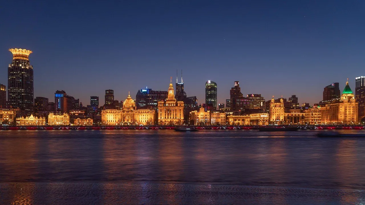 Fachadas históricas iluminadas do Bund vistas através do Huangpu sob céu azul-escuro.