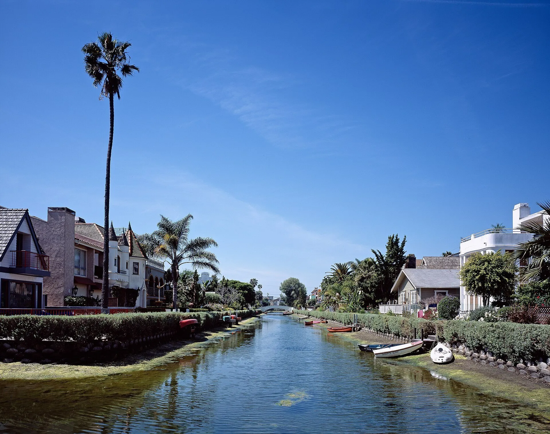 Canal de Venice, em Los Angeles, entre casas e palmeiras, com pequenos barcos e ponte branca ao fundo.