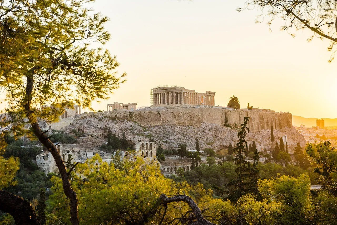 Acrópole e Partenon entre pinheiros, iluminados pelo sol do fim da tarde em Atenas.