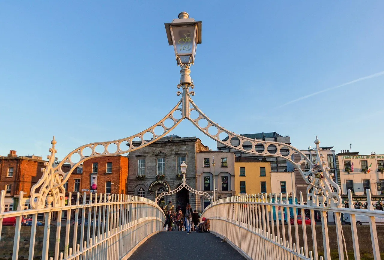 Passarela branca da Ha’penny Bridge com pedestres e fachadas coloridas ao fundo, em Dublin.