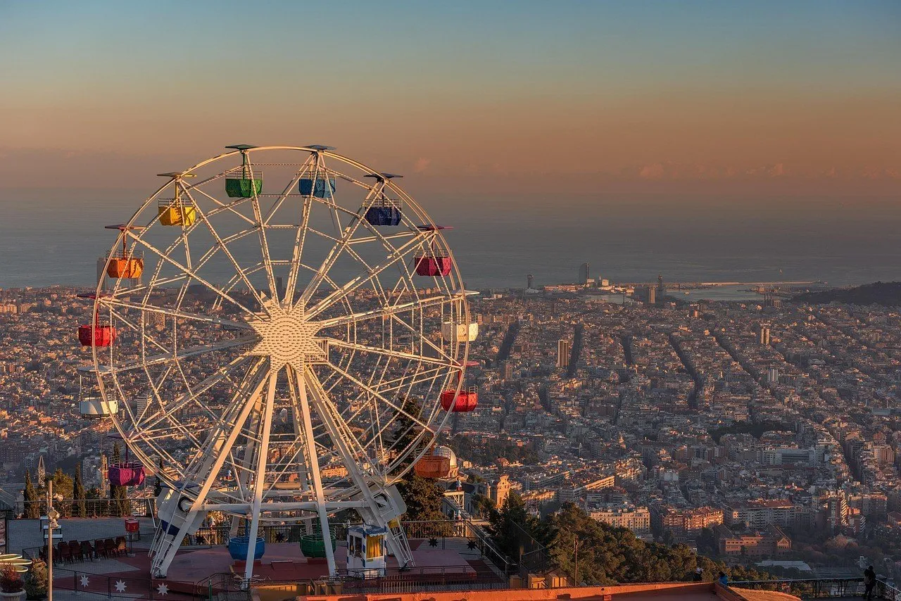Roda-gigante do Tibidabo em primeiro plano, com Barcelona e o Mediterrâneo sob luz dourada.