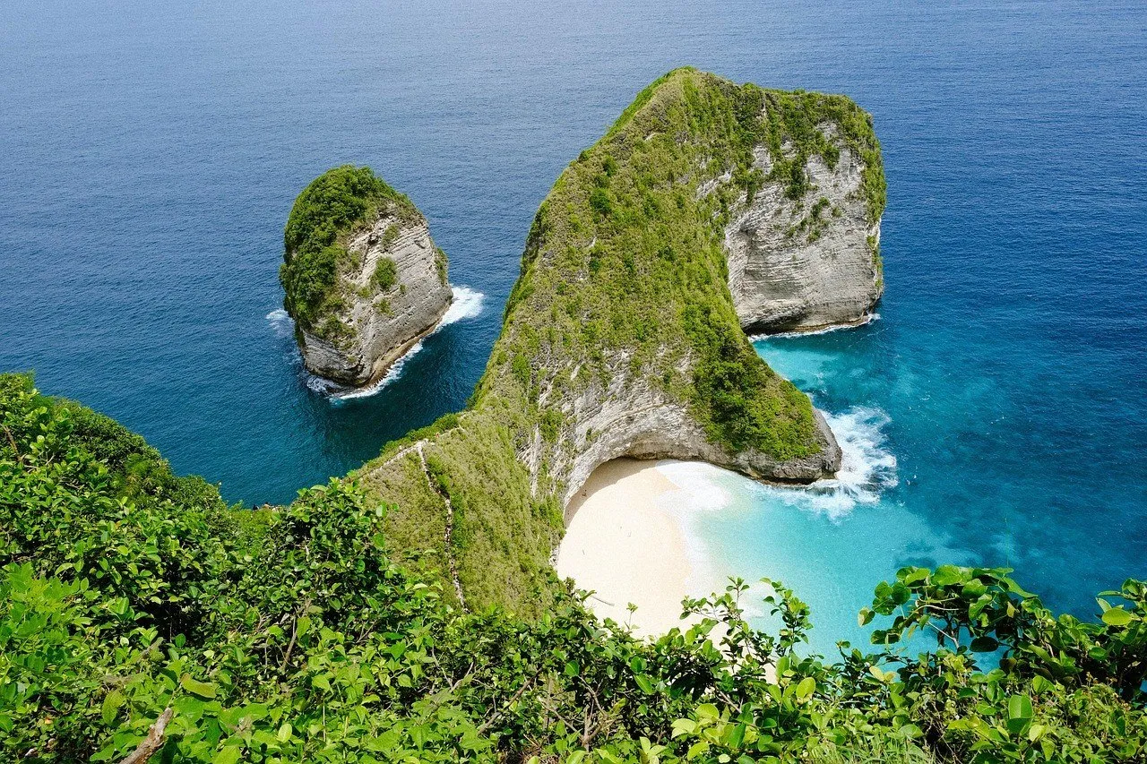 Falésia verde de Kelingking vista do alto, com areia clara, mar turquesa e um rochedo ao lado, em Nusa Penida.