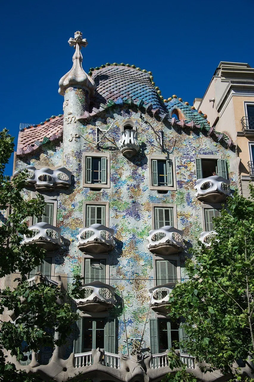 Fachada da Casa Batlló com varandas curvas, mosaicos e telhado de cerâmica sob céu azul.