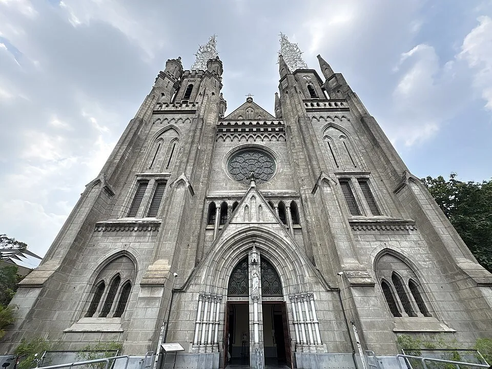 Fachada externa da Catedral de Jacarta, com rosácea central e torres neogóticas vistas de baixo.