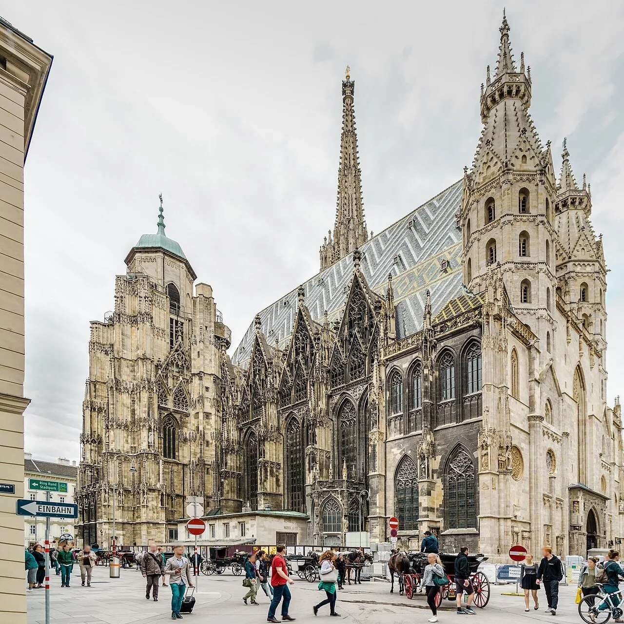 Fachada e telhado de telhas coloridas da Stephansdom, com torres e pessoas na praça.