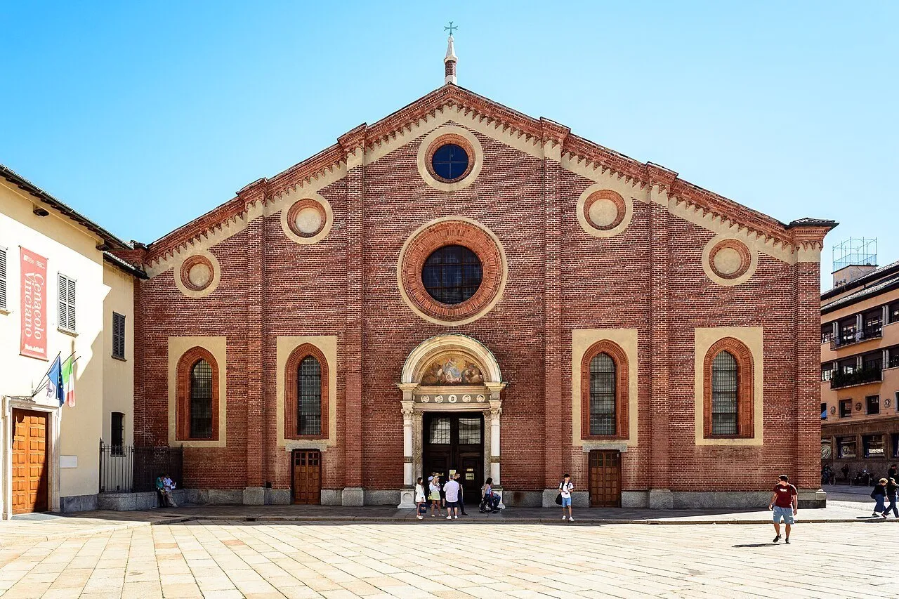 Fachada de tijolos de Santa Maria delle Grazie, em Milão, com janelas circulares e visitantes na praça.