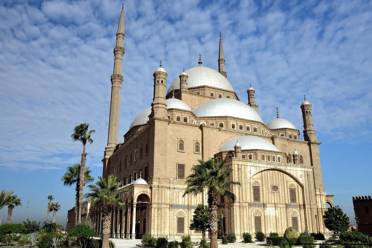Exterior da Mesquita de Muhammad Ali na Cidadela do Cairo, com cúpulas claras, minaretes e palmeiras.