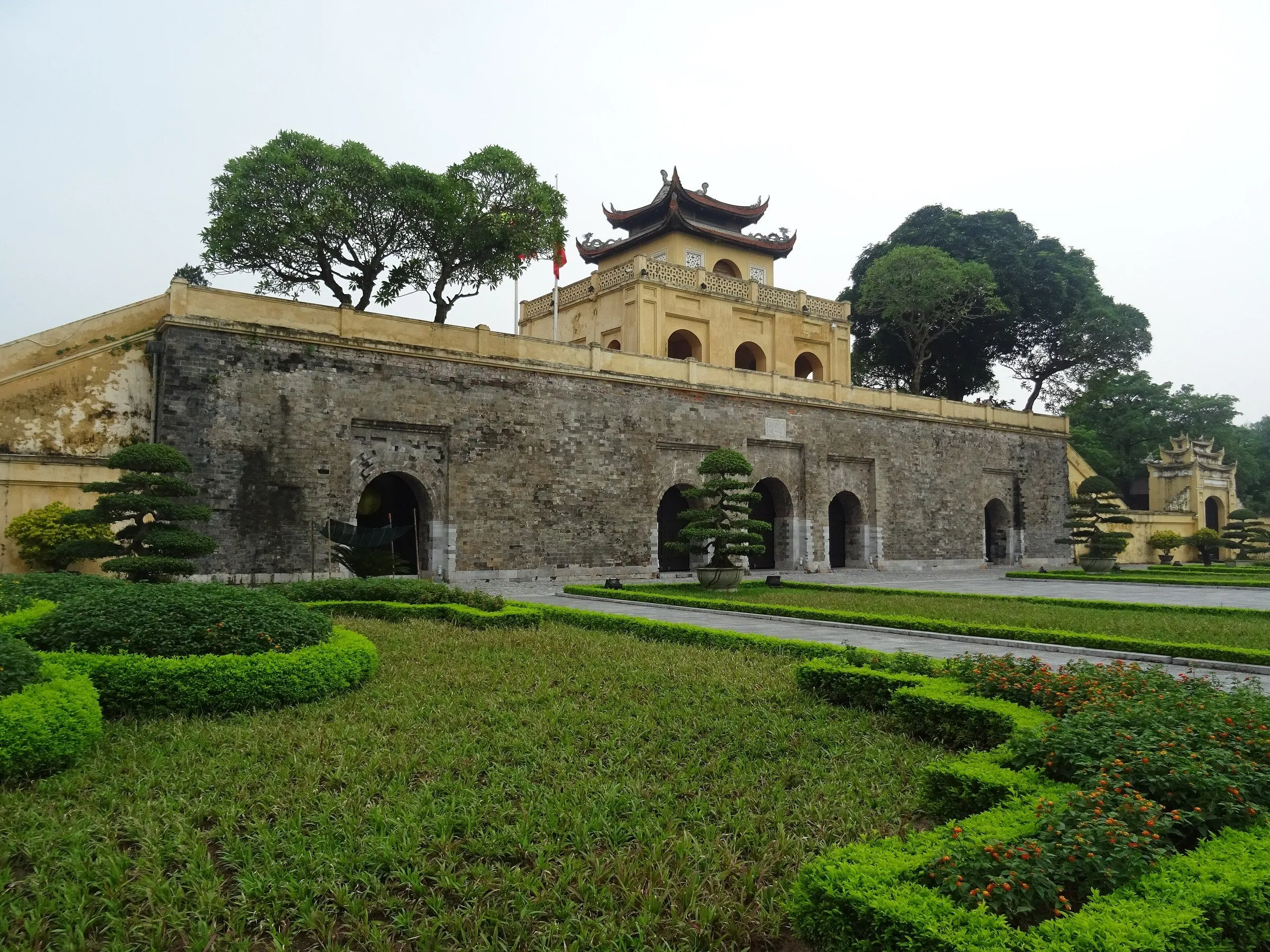 Portão Doan Mon da Cidadela Imperial Thang Long, com muralha de tijolos e jardins à frente.