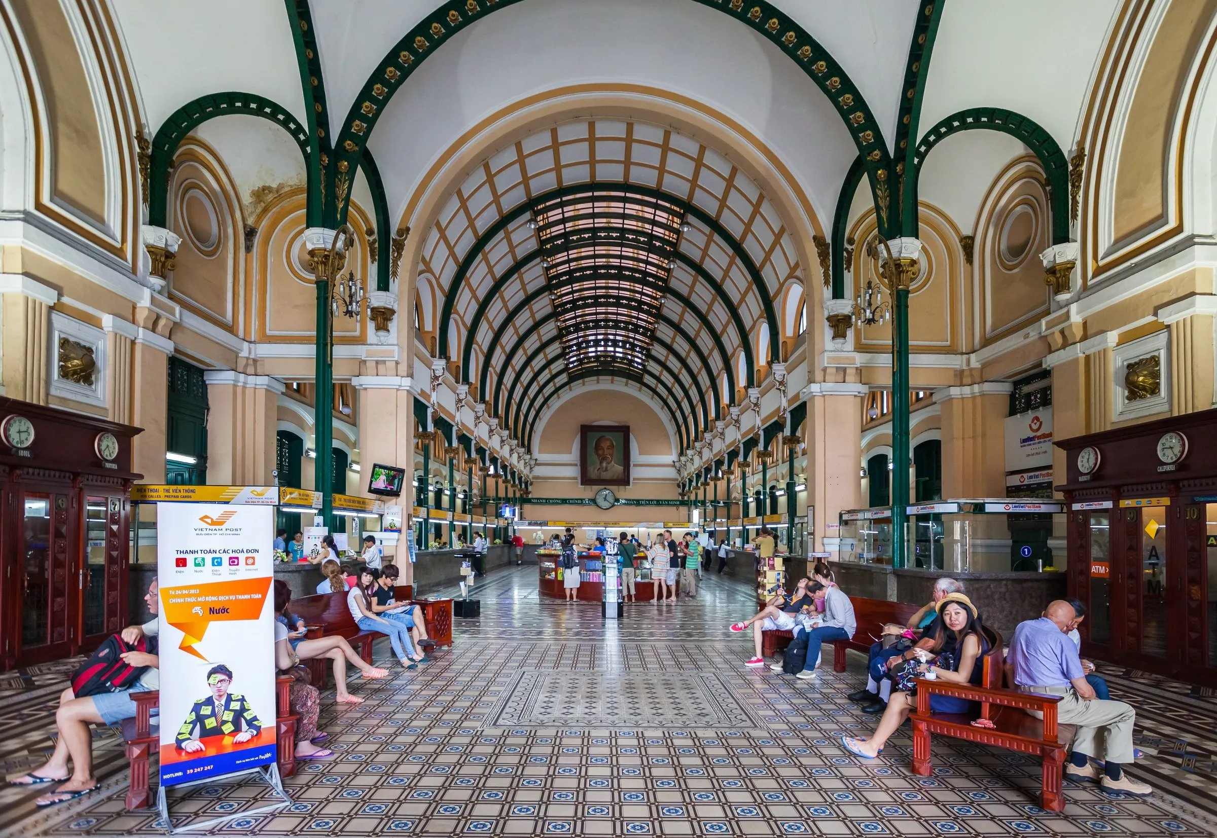 Salão dos Correios Centrais de Saigon com teto abobadado, piso geométrico, balcões e bancos laterais.