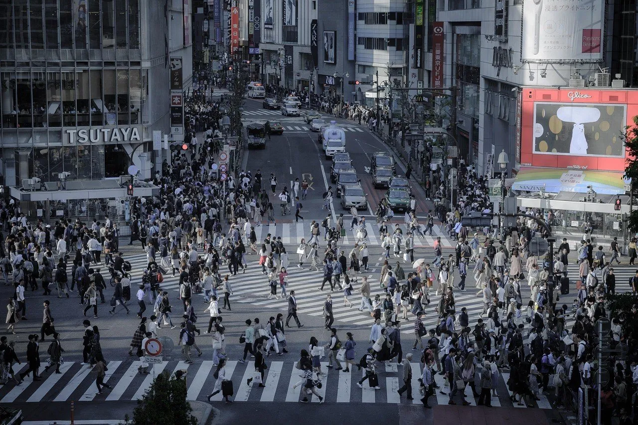 Cruzamento de Shibuya visto do alto, com faixas diagonais, muitos pedestres e fachadas comerciais.