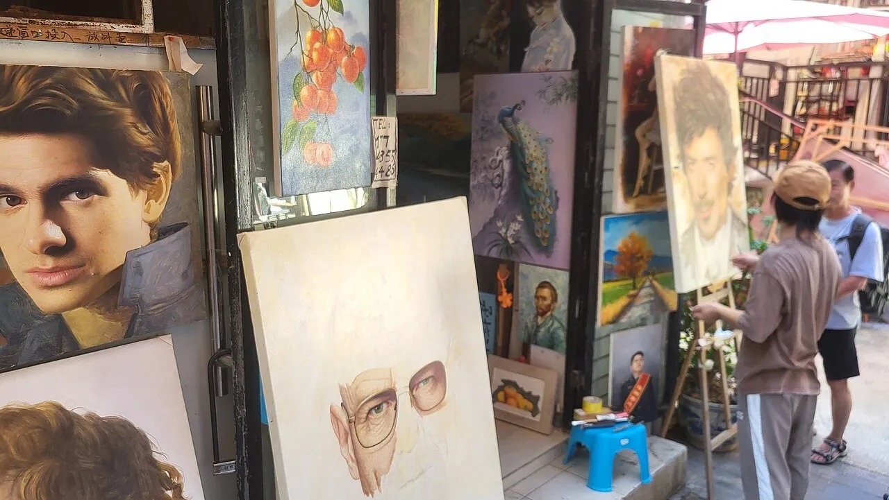 Galeria de Dafen com vários quadros expostos na entrada e um pintor de costas trabalhando em um cavalete.