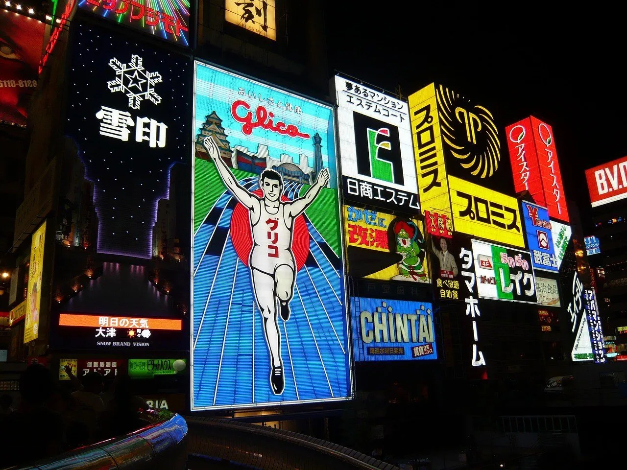 Painel luminoso do corredor da Glico à noite, cercado por anúncios coloridos em Dotonbori.