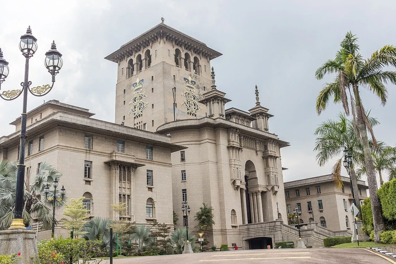 Exterior do Edifício Sultan Ibrahim, com torre de pedra clara, palmeiras e postes decorativos.