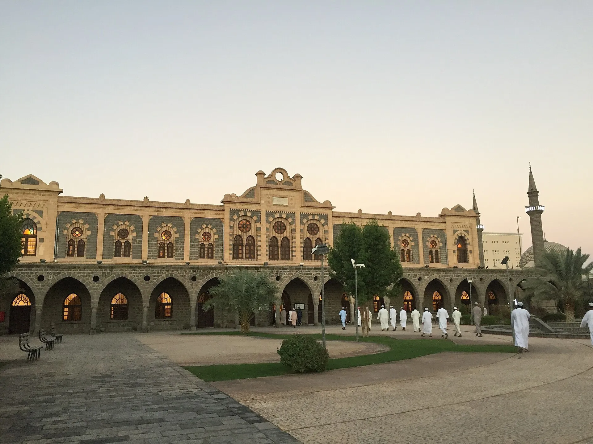 Fachada de pedra da antiga estação de Hejaz em Medina, com arcos, janelas iluminadas e palmeiras.
