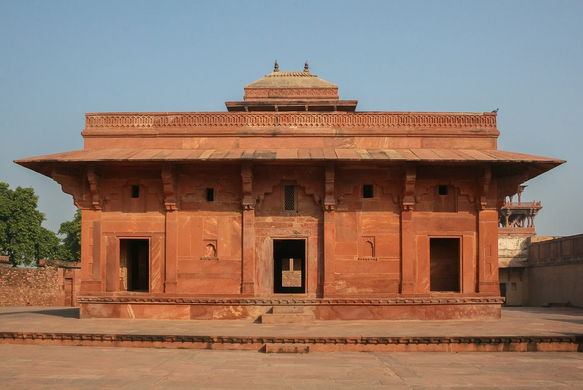 Edifício palaciano de arenito vermelho em Fatehpur Sikri, com portas escuras e pátio sem visitantes.