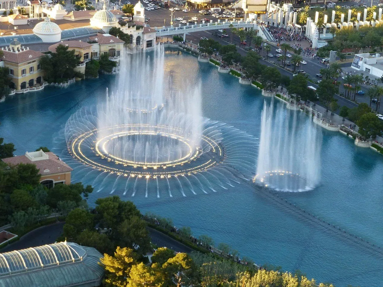 Jatos de água e círculos iluminados no lago do Bellagio, vistos de um ponto elevado ao entardecer.