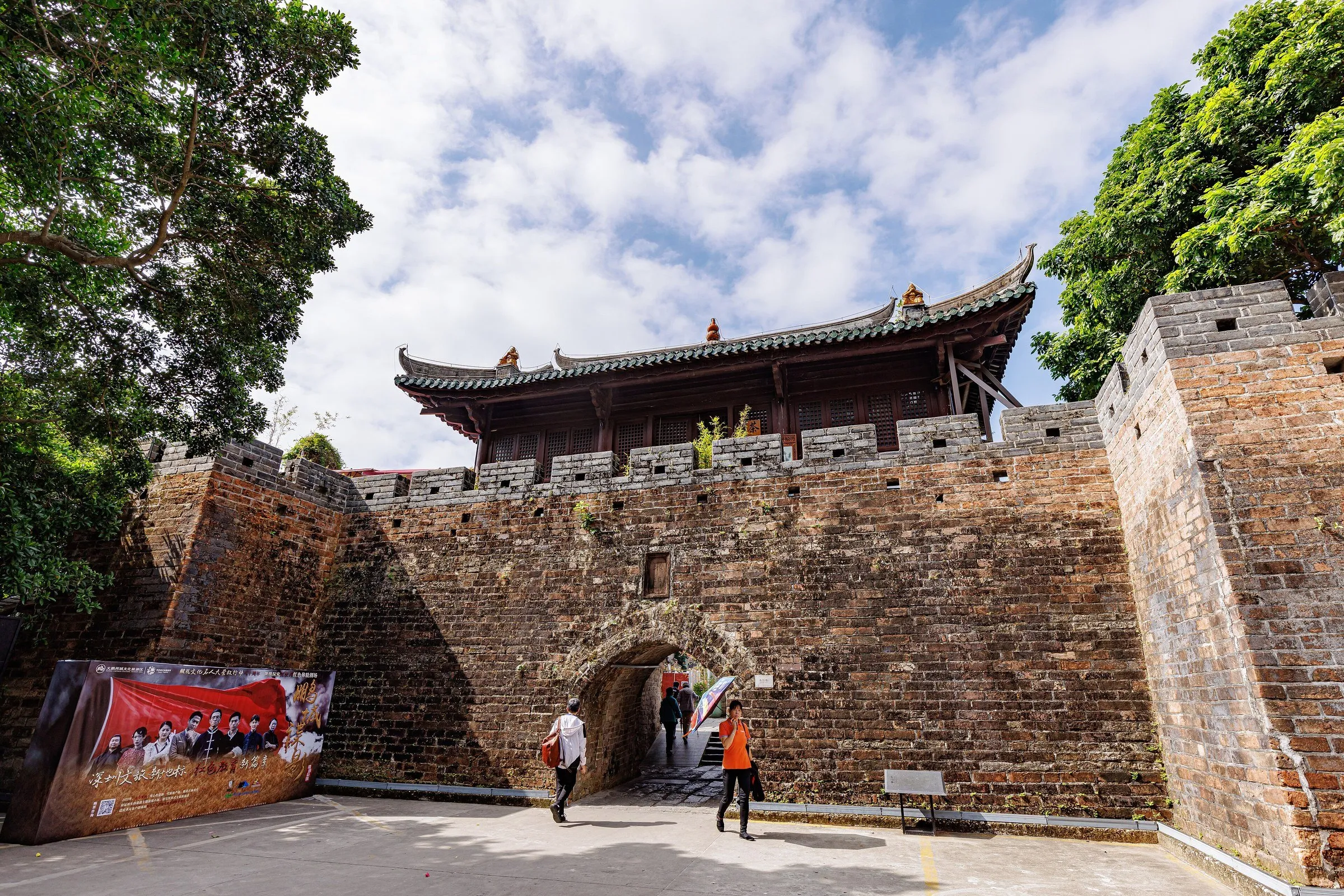 Muralha de tijolos e torre do portão da fortaleza de Dapeng, sob céu azul com nuvens.