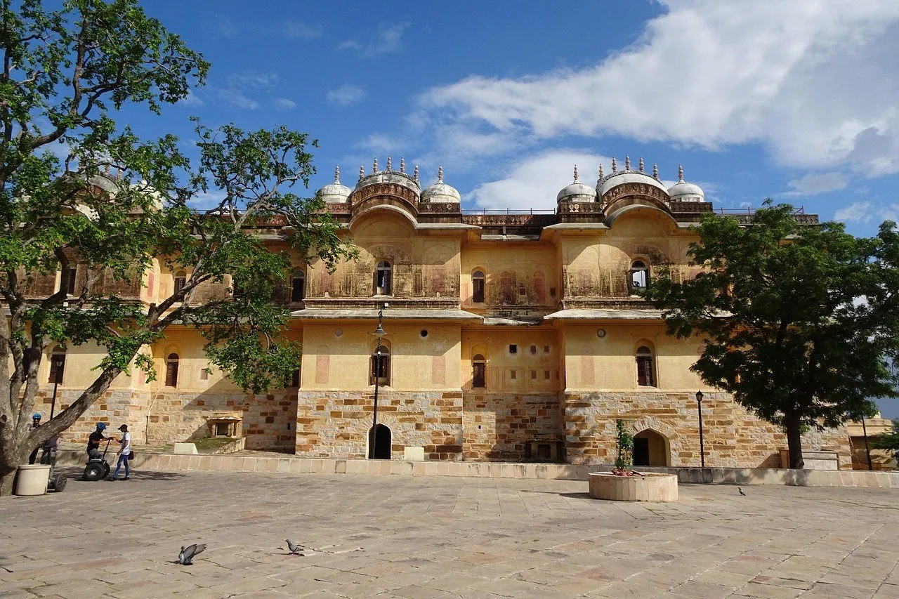 Fachada amarela do Madhavendra Bhawan, em Nahargarh, entre árvores e um pátio de pedra.