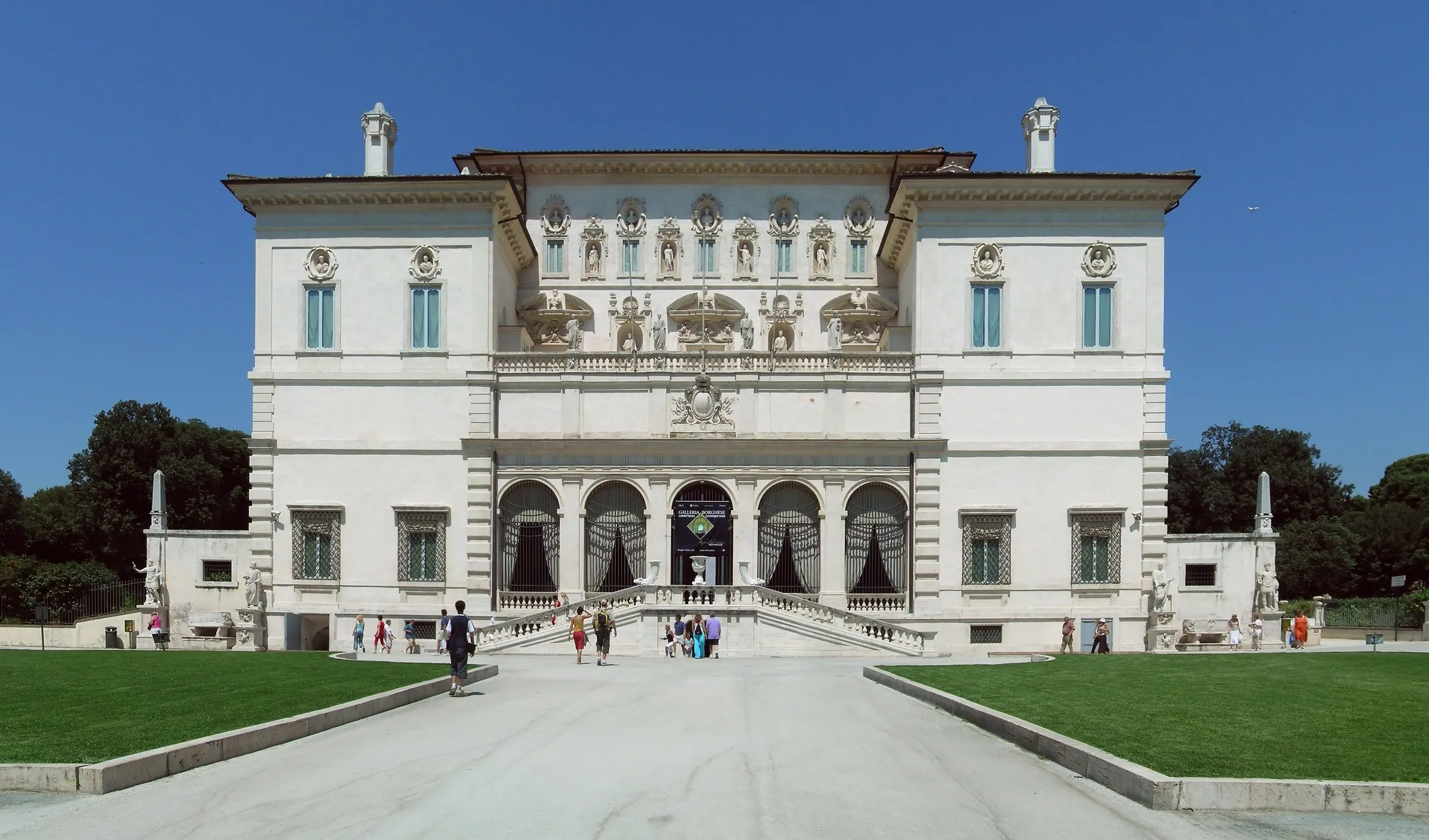 Fachada branca da Galleria Borghese, com escadaria de entrada e gramado em primeiro plano sob céu azul.