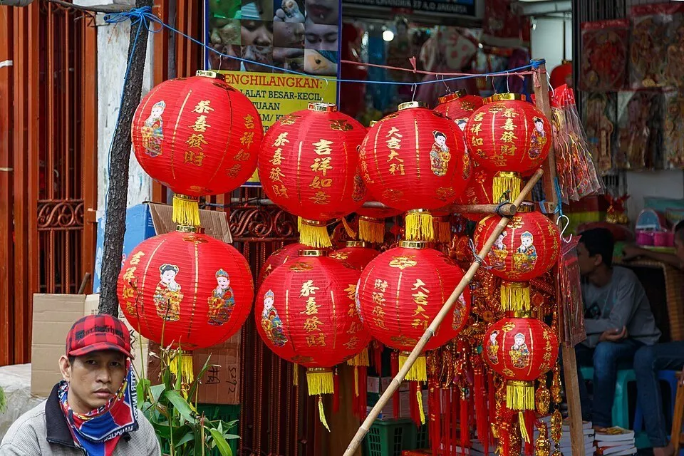 Lanternas chinesas vermelhas e douradas expostas numa banca de Glodok, com vendedores nas bordas.