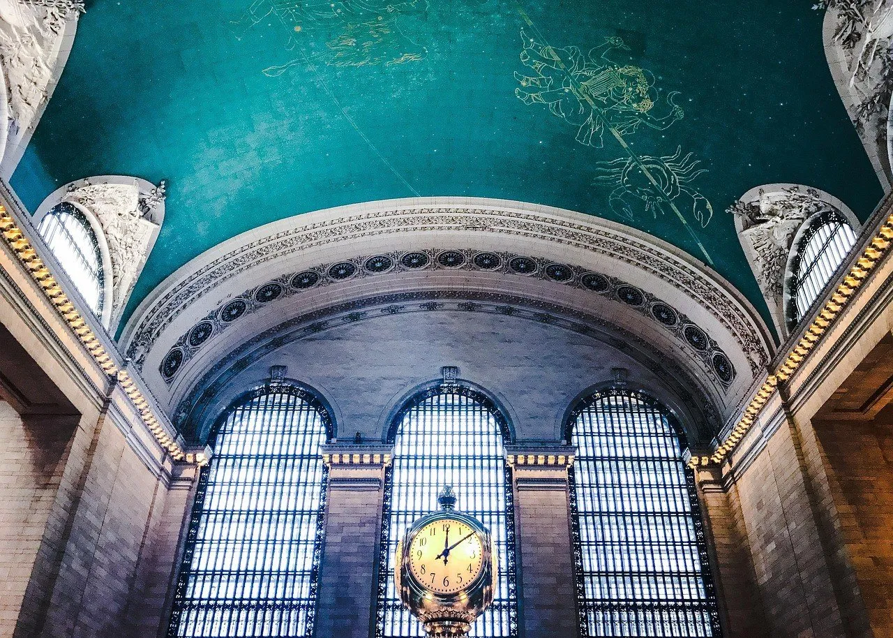 Teto verde-azulado com constelações pintadas no saguão da Grand Central, com janelas em arco e um relógio dourado.