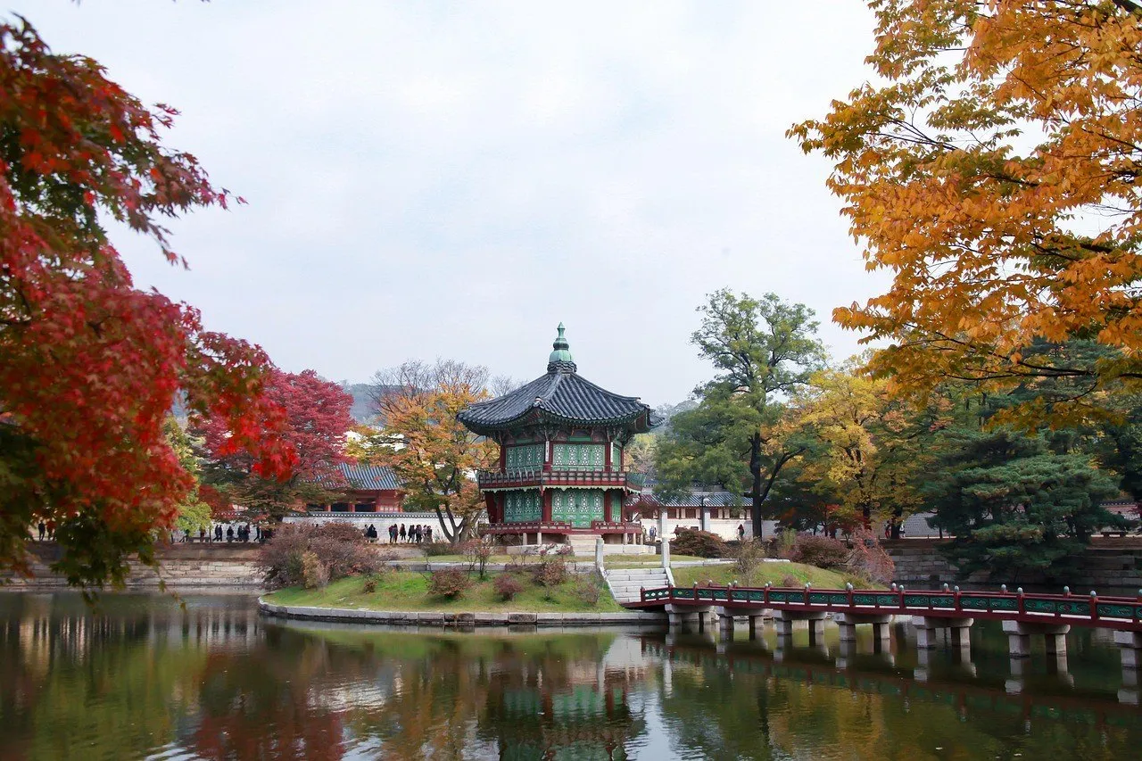 Pavilhão de Gyeongbokgung junto a um lago, cercado por árvores com folhas de outono.