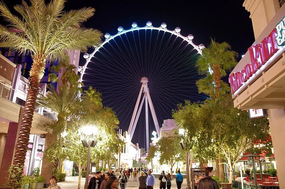 High Roller iluminado à noite no fim da LINQ Promenade, entre palmeiras, lojas e pedestres.