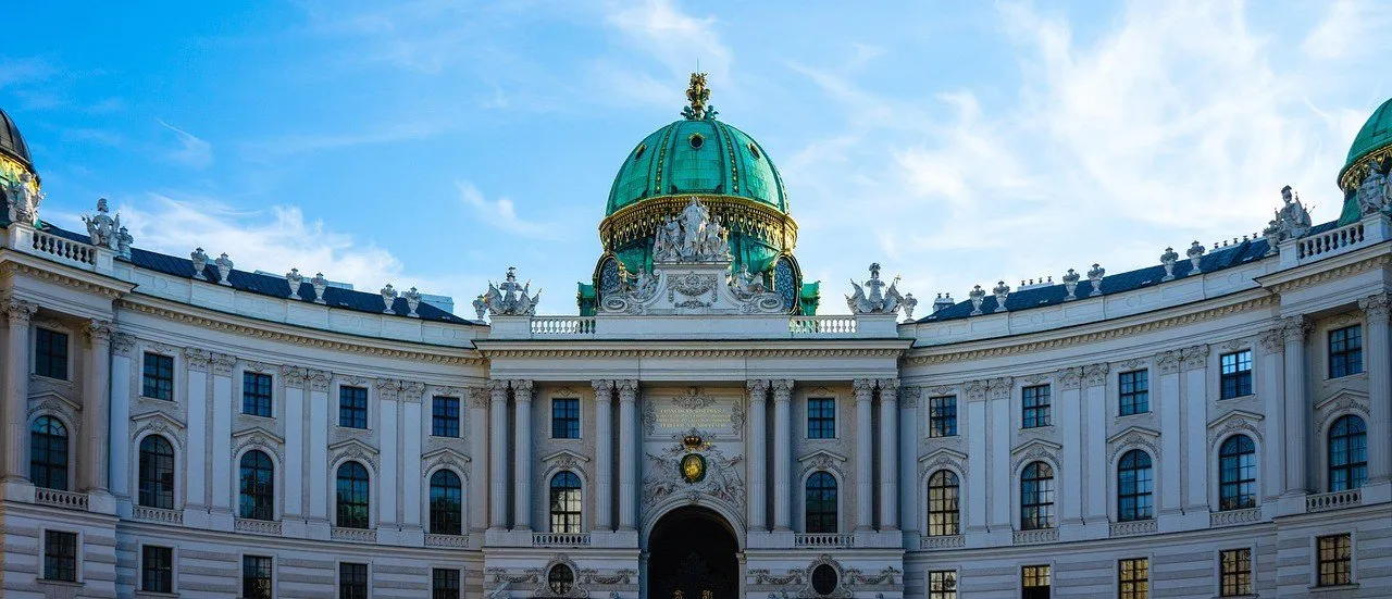Fachada curva da Hofburg com janelas, esculturas e cúpula verde, vista da Michaelerplatz.
