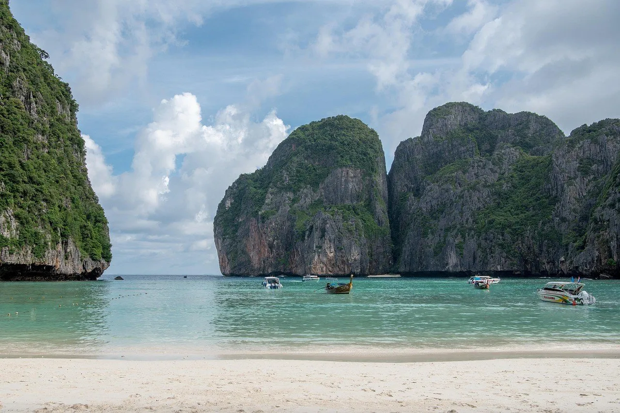 Maya Bay, nas ilhas Phi Phi, com paredões de calcário cobertos de mata, barcos ao longe, água clara e areia branca.