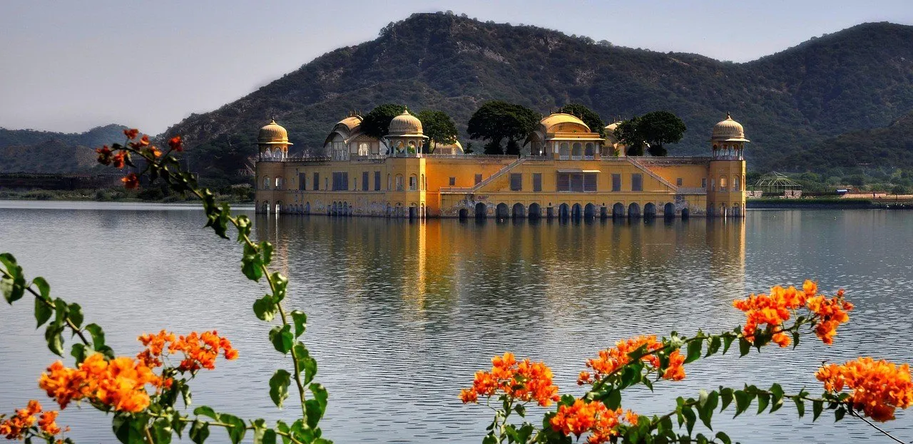 Jal Mahal refletido no lago Man Sagar, com flores alaranjadas à frente e colinas ao fundo.