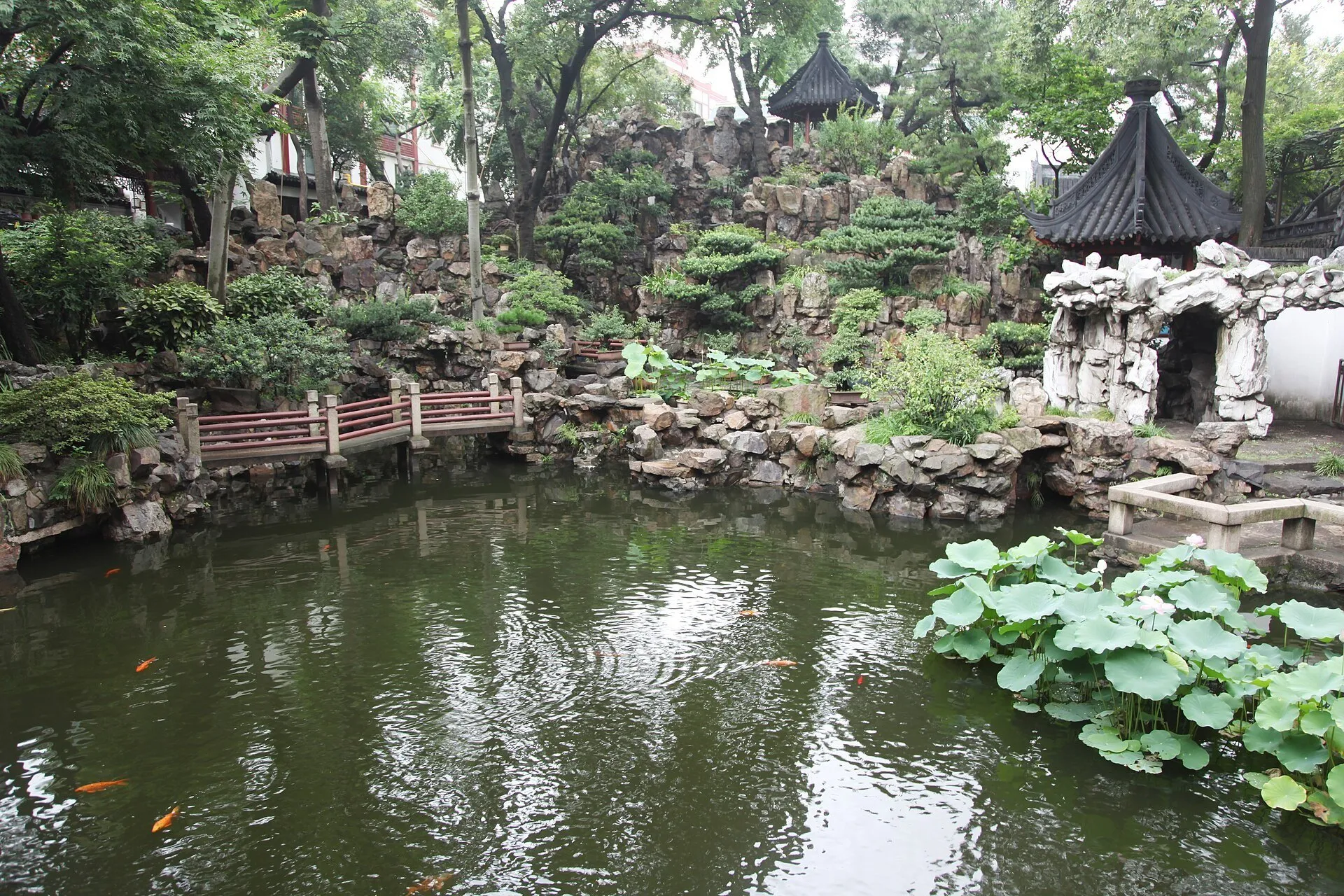 Lago com carpas, rochas, árvores e pavilhões de telhas escuras no interior do Jardim Yu.