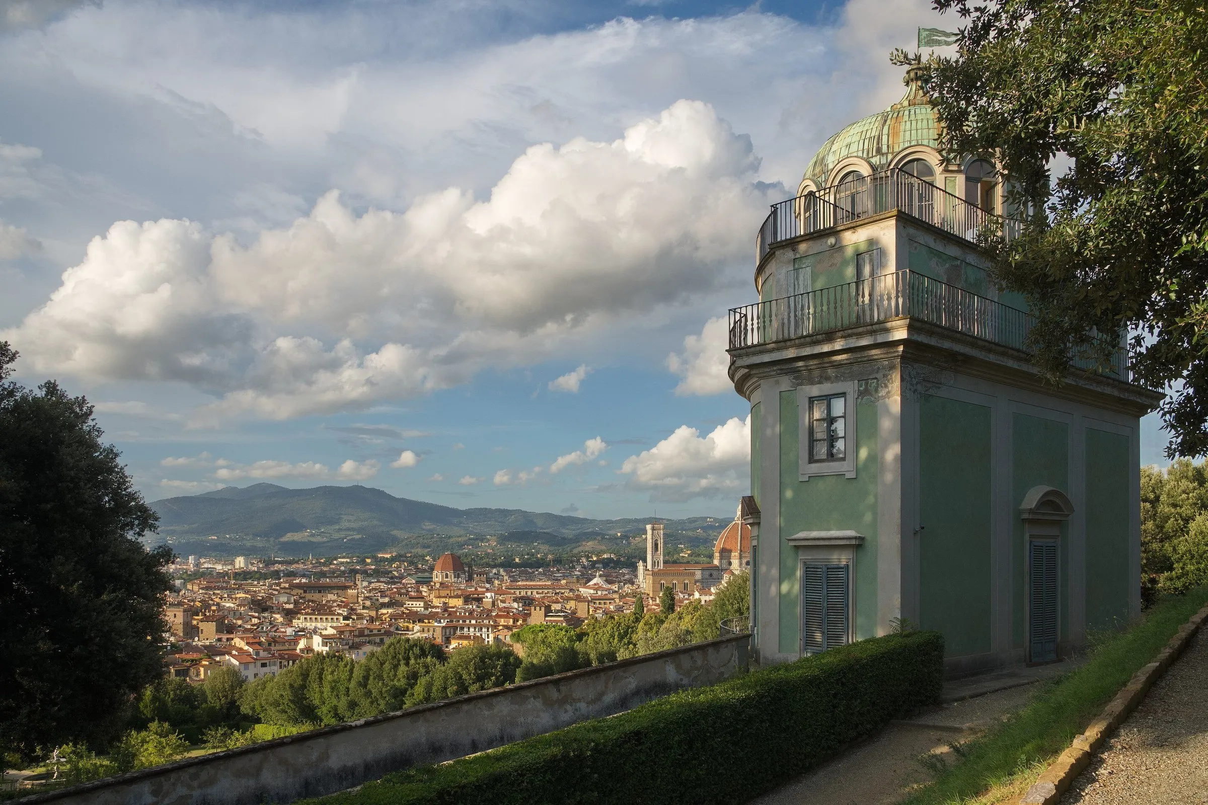 Pavilhão verde dos Jardins de Boboli, com sebes, árvores e panorama de Florença ao fundo.