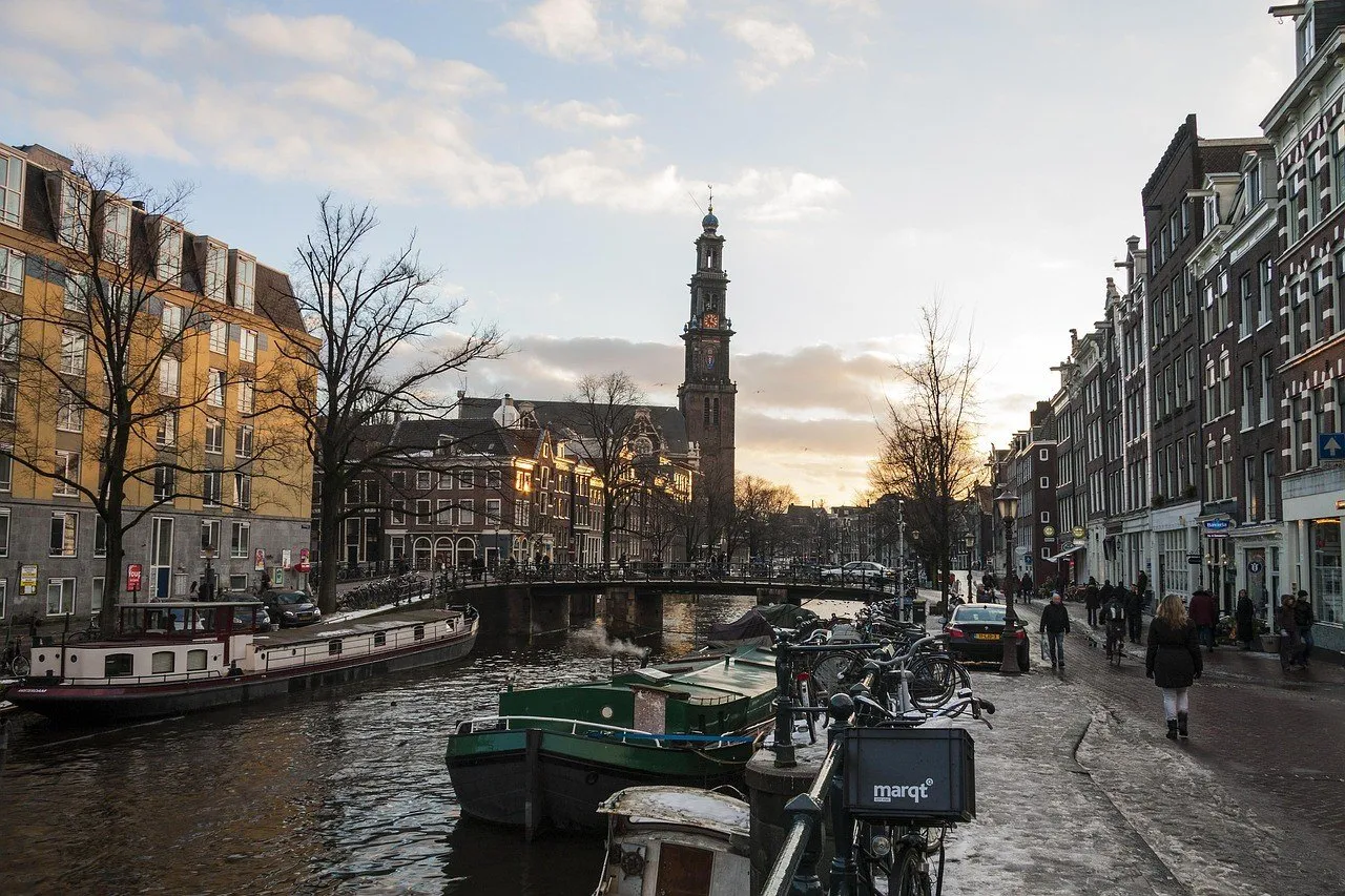 Canal com barcos e bicicletas junto ao Jordaan, com ponte e torre da Westerkerk ao fundo.