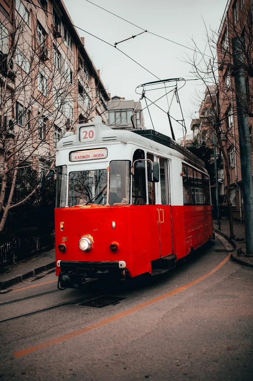 Bondinho vermelho e branco com a placa Kadıköy–Moda numa rua do bairro, entre prédios e árvores sem folhas.
