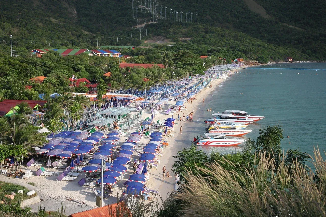 Praia de Koh Larn vista do alto, com guarda-sóis, lanchas junto à areia e encosta verde.