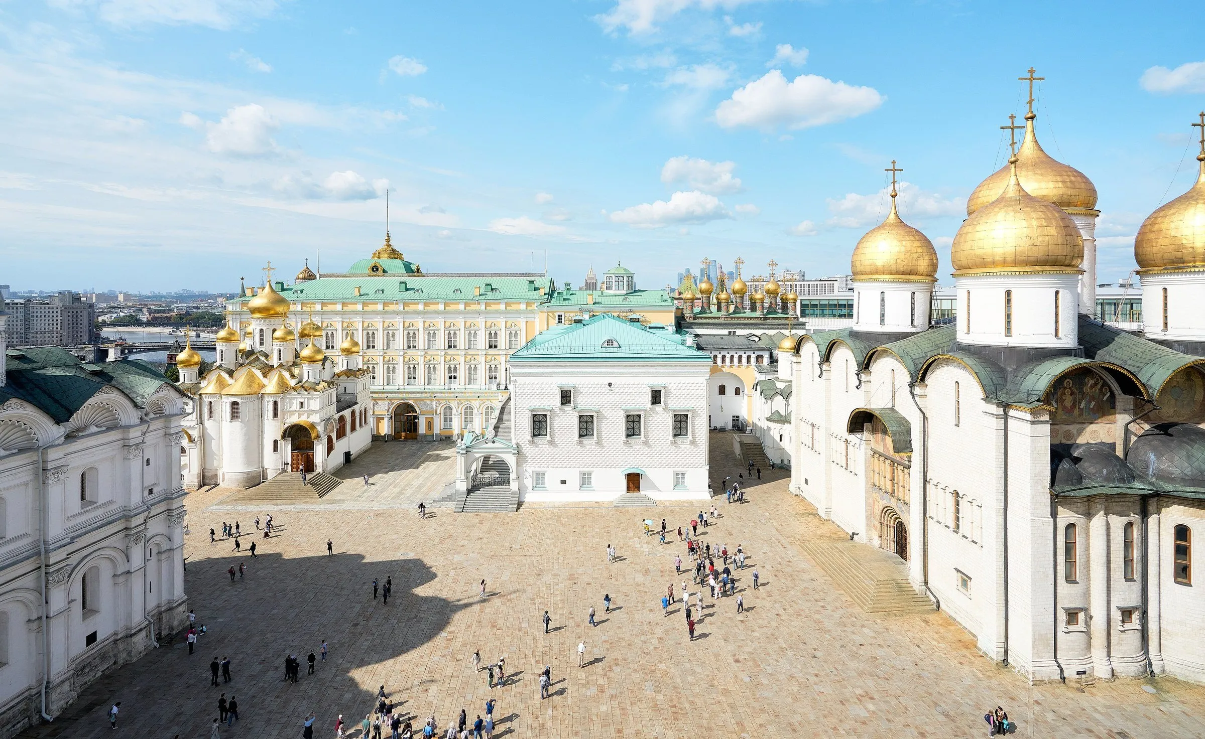 Vista elevada da Praça das Catedrais no Kremlin, com igrejas brancas, cúpulas douradas e visitantes.