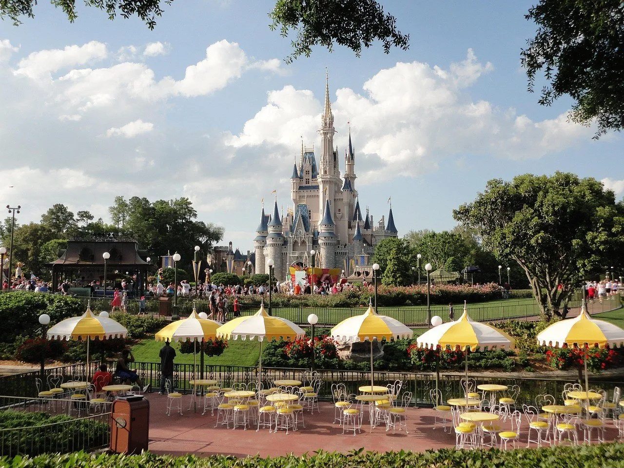 Castelo da Cinderela ao fundo de jardins, mesas e guarda-sóis amarelos no Magic Kingdom.