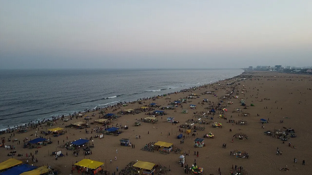 Vista aérea da Marina Beach ao anoitecer, com barracas coloridas, visitantes, faixa de areia e mar.