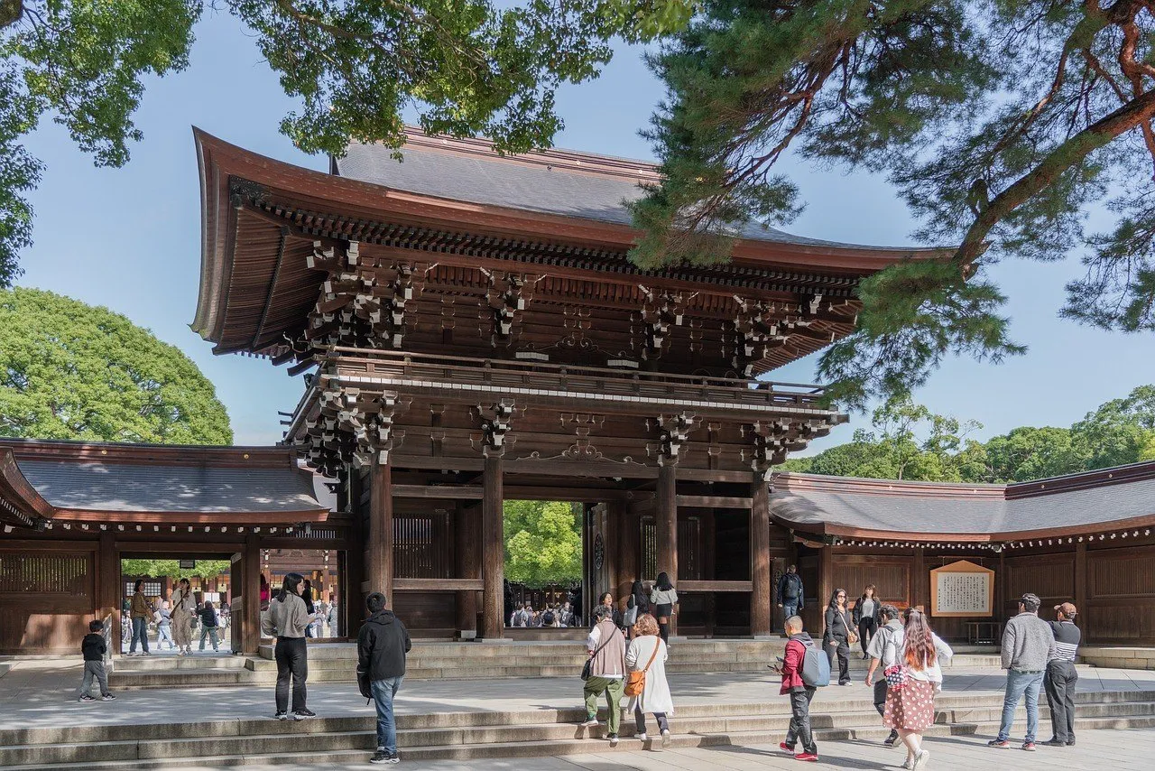 Portão de madeira do Meiji Jingu, com árvores e visitantes no pátio sob luz do dia.
