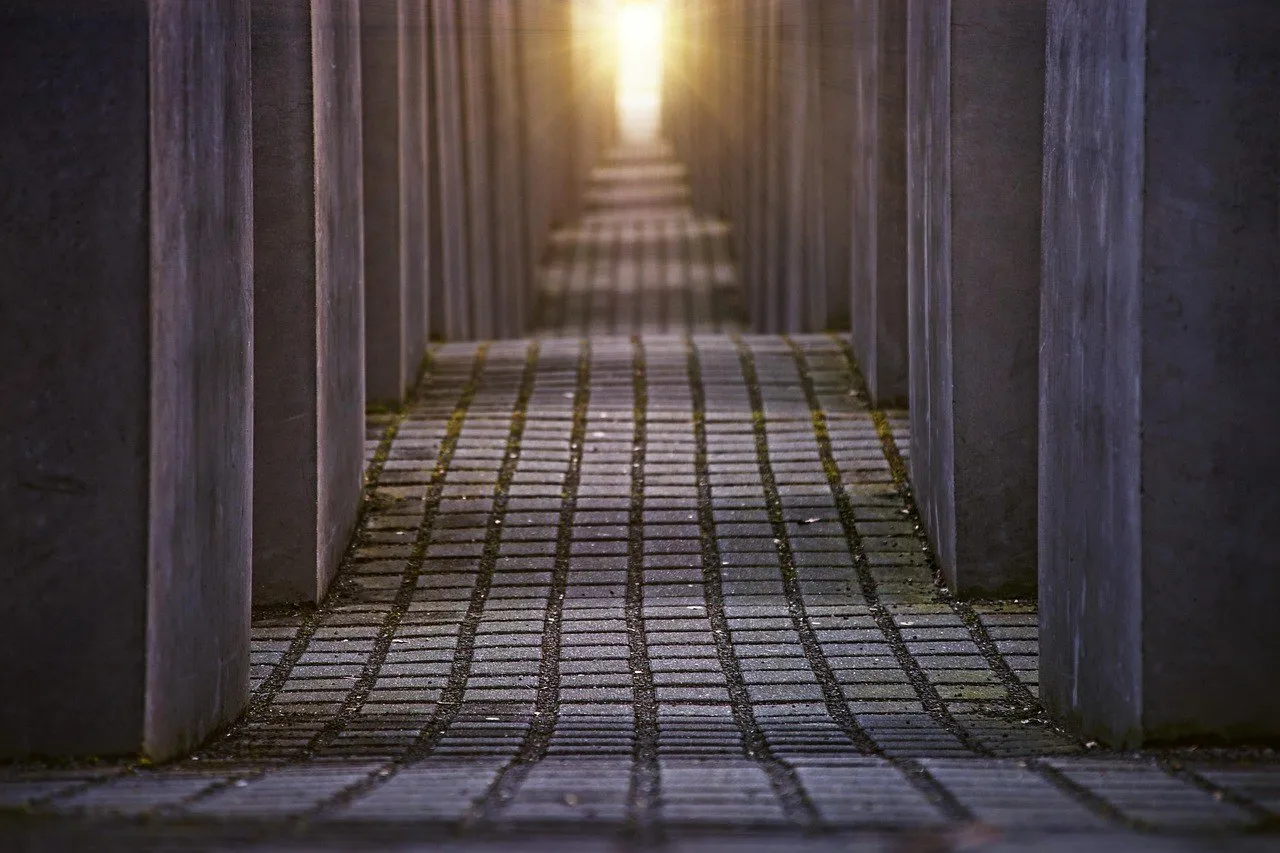 Corredor de pedras entre estelas de concreto do Memorial do Holocausto, com luz ao fundo.