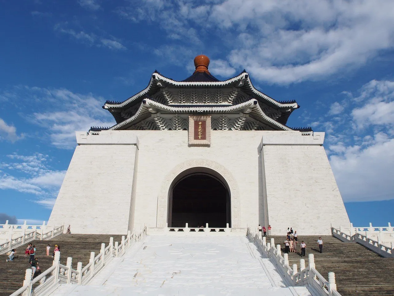 Fachada branca e telhado azul do Memorial Chiang Kai-shek, vistos da base das escadarias sob céu azul.