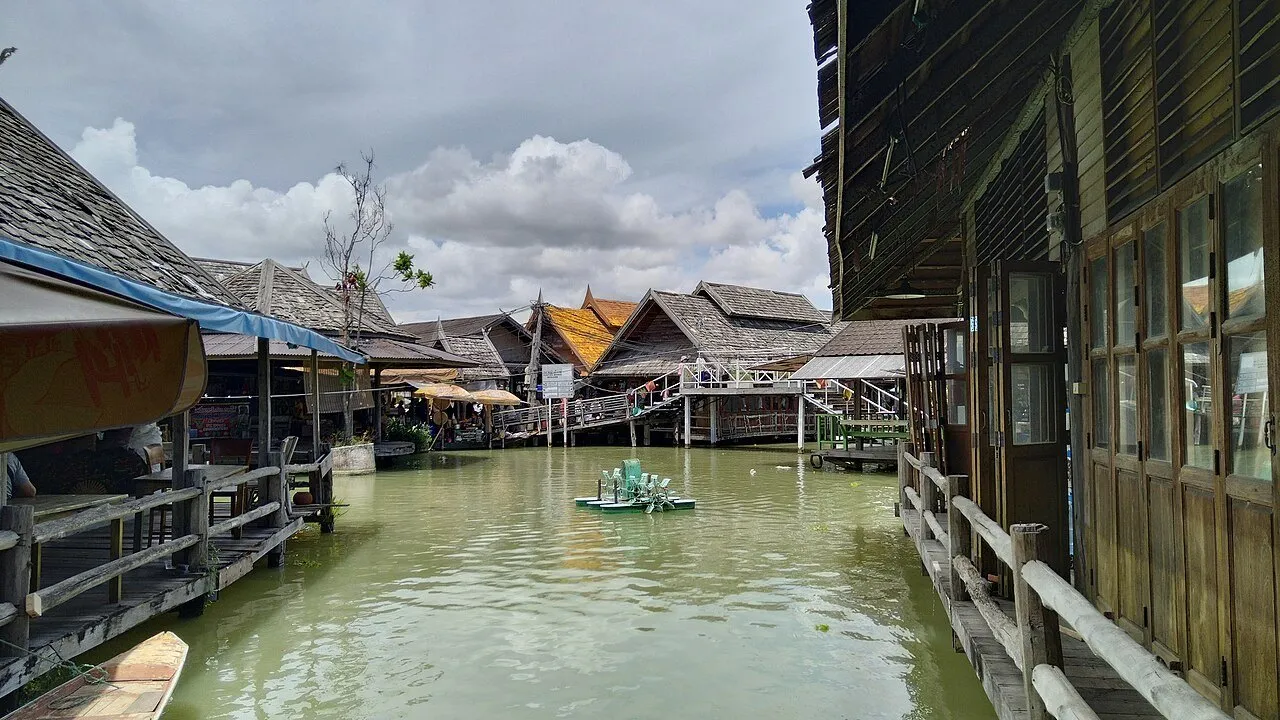 Casas e passarelas de madeira junto à água verde do Mercado Flutuante de Pattaya, com telhados ao fundo.