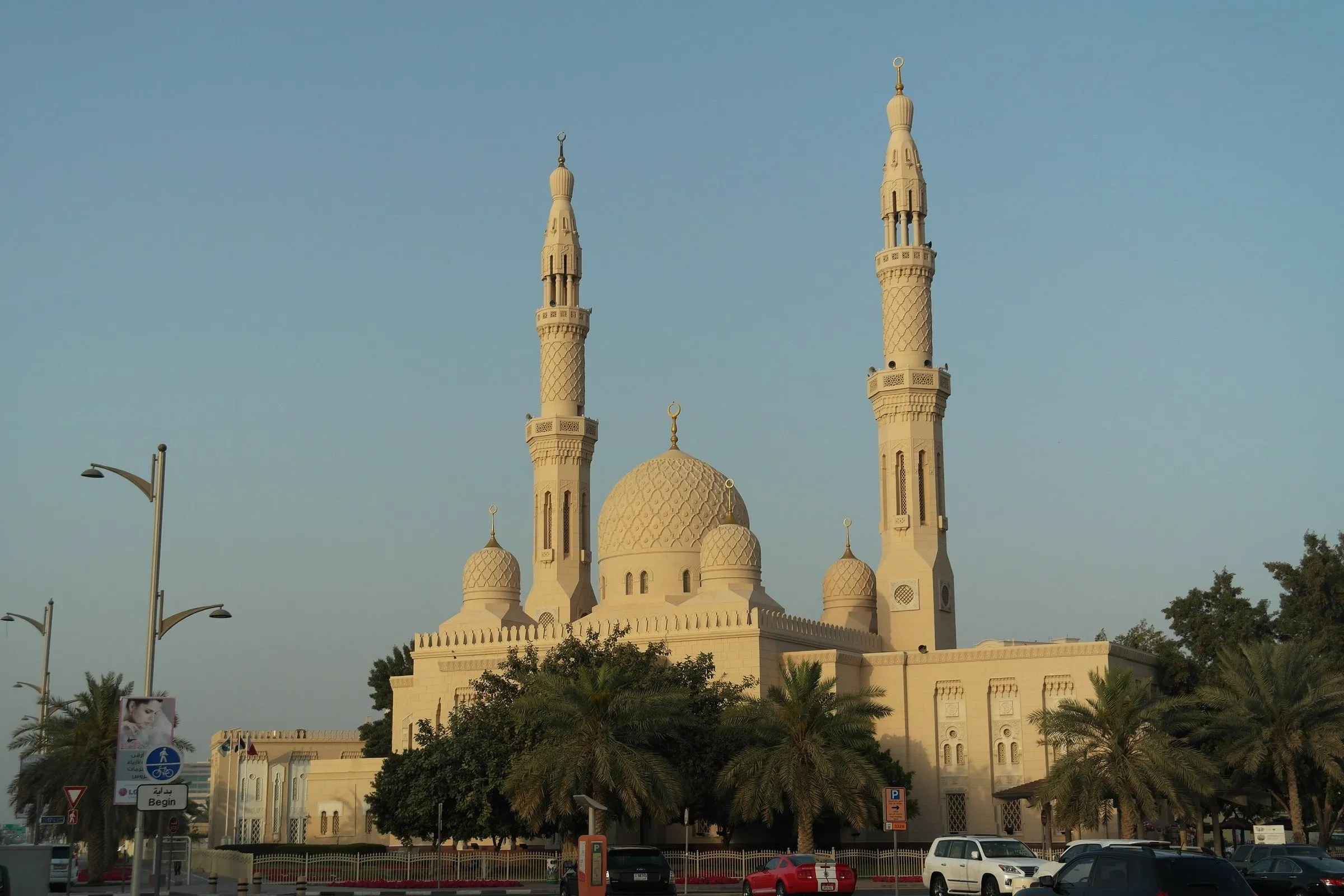 Mesquita de Jumeirah inteira, com dois minaretes e cúpulas de pedra clara entre palmeiras, na luz dourada do fim da tarde.