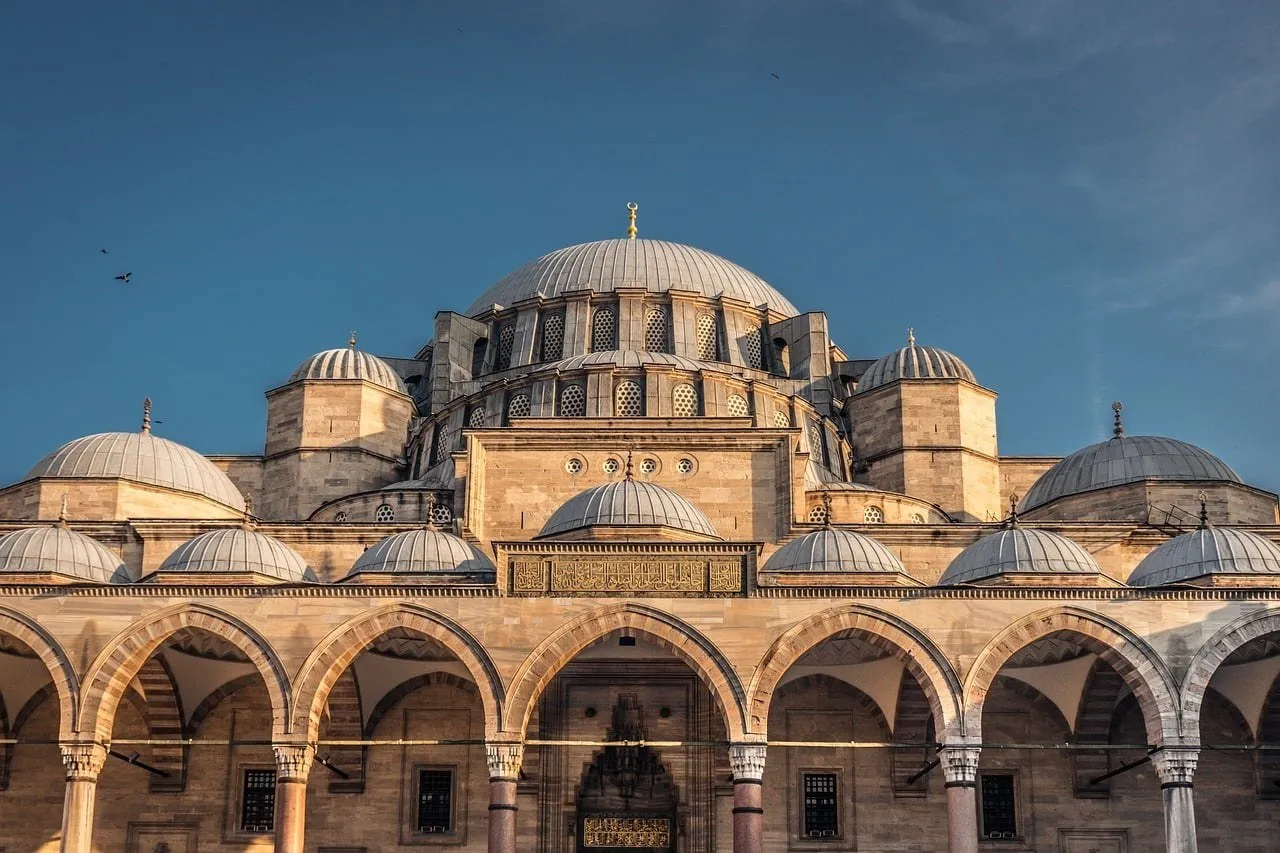 Cúpula central e cúpulas menores da Mesquita de Süleymaniye vistas do pátio, com arcadas de pedra em primeiro plano.